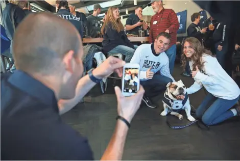  ?? MICHAEL SEARS / MILWAUKEE JOURNAL SENTINEL ?? Michael Kaltenmark (left) of Indianapol­is, the handler for Butler Blue III, takes photos of Joel Cohen and his daughter, Caroline Cohen, a student at Butler, at Evolution Gastro Pong, 1023 N. Old World 3rd St. The English bulldog is the mascot for...