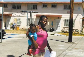  ?? Mel Melcon / Los Angeles Times ?? A mother carries her daughter at the Ramona Gardens housing project in Los Angeles. Latino gang members admit carrying out a racially motivated attack on black families at the complex.