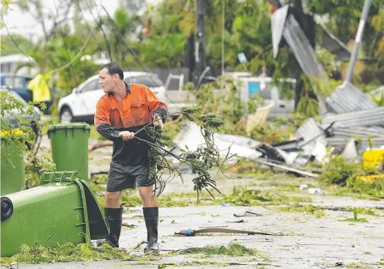  ?? . ?? ONSLAUGHT: A resident helps clear debris from the road after the mini tornado swept through Townsville and (below) one of the homes destroyed in the storm.