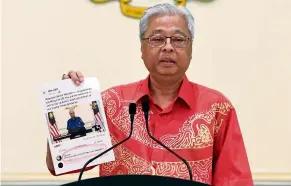  ??  ?? Not true: Ismail Sabri showing a printed screencap of a social media post which claimed that he did not welcome Singaporea­ns to Malaysia. — Bernama