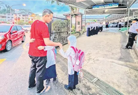  ?? — Photo by Roystein Emmor ?? Civil servant Adi Lukman Ali Hassan sends off his daughters Ayra Irdina, 7, and Aryana Nur Imani, 9, at SK St Mary in Kuching.