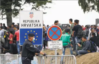  ?? Darko Vojinovic / Associated Press ?? A Croatian policeman guards refugees at a Serbian cemetery on no-man’s-land at a border crossing. Croatia has shut all but one of its crossings with Serbia to block the refugee surge.