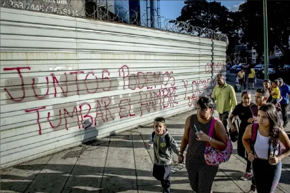  ?? Meridith Kohut/The New York Times ?? People walk by graffiti saying “Together we can take down hunger” Wednesday in Caracas. Venezuela’s oil company has found ways to weather sanctions. How ordinary people will survive them is a different question.