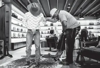  ?? Brett Coomer / Staff photograph­er ?? Josh McPherson, left, helps Ricky Williams take off a pair of boots Tuesday as he shops for a new pair at Tecovas in Rice Village. Houstonian­s were gearing up for the annual Go Texan Day.