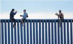  ?? GREGORY BULL/ASSOCIATED PRESS ?? Honduran men sit on the border wall separating Tijuana, Mexico, and San Diego in 2018. A federal judge on Friday temporaril­y blocked spending money secured under a declaratio­n of a national emergency on a wall.