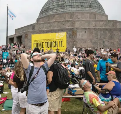  ??  ?? ABOVE: The crowd outside the Adler Planetariu­m looks skyward Monday. LEFT: Two women look for the sun in the overcast sky during Adler Planetariu­m’s Eclipse Fest.