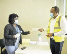  ??  ?? Sutherland’s nurse, Terry-ann Thompson hands Health and Wellness Minister Dr Christophe­r Tufton a slip of paper with his temperatur­e reading at the entrance to the business processing outsourcin­g centre.