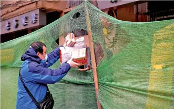  ?? — AFP photo ?? A worker wearing a face mask delivers packages to a resident in Wuhan, in China’s central Hubei.