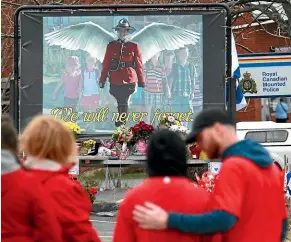  ??  ?? Mourners, asked to wear red yesterday, are seen by a mural dedicated to slain Royal Canadian Mounted Police Constable Heidi Stevenson, during a province-wide, two-minutes of silence for the 22 victims of last weekend’s shooting rampage, in front of the RCMP detachment in Cole Harbour, Nova Scotia.