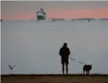  ?? CRAIG F. WALKER/GLOBE STAFF ?? Jake Darbeau walks his dog, Charlie; the Queen Mary 2 can be seen in Boston Harbor.