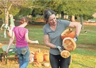  ?? ?? Fifth-generation farmer Katherine Harrison, right, who owns the Harrison Farm, gathers up chunks of pumpkins to feed to the farm’s herd of sheep with help from volunteer Lauren Kurtz.