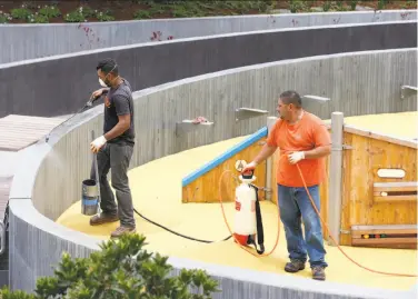  ?? Paul Chinn / The Chronicle ?? Alberto Maya (left) and Hector Acosta spray a weather sealant on concrete for the playground this week.