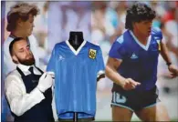  ?? (AFP) ?? A file photo taken on April 20, 2022 a Sotheby’s technician adjusts a football shirt worn by Argentina’s Diego Maradona during the 1986 World Cup quarter-final match against England, during a photocall at Sotheby’s auction house in London ahead of its sale.