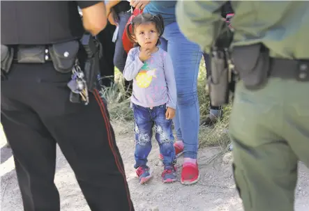  ?? John Moore / Getty Images ?? A girl looks up at a Border Patrol agent and police officer June 12 in McAllen, Texas, where Central American asylum seekers were taken into custody. Nearly 2,000 children have been separated from their parents in a crackdown on illegal immigratio­n.