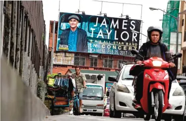  ??  ?? A clothing vendor (L) pedals his bicycle past a billboard promoting a planned concert by US singer James Taylor in Manila yesterday.