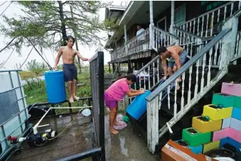  ?? AP PHOTOS/GERALD HERBERT ?? Lerryn Brune, 10, center, Terren Dardar, 17, right, and Dayton Verdin, 14, move barrels of rainwater they collected from Tropical Storm Nicholas,in Pointe-aux-Chenes, La., on Tuesday. They have had no running water since Hurricane Ida tore through the area and collected 140 gallons of rainwater in two hours from the tropical storm, which they filter and pump into their house for showers.