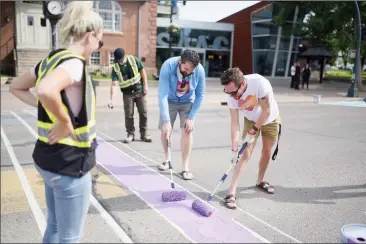  ?? Herald photo by Tijana Martin ?? Lethbridge Pride Fest Society members Nick Antson and Adam Saley, right, help paint the rainbow LGBTQ+ flag on the crosswalk along 3 Avenue and 6 Street South on Thursday. @TMartinHer­ald