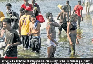  ??  ?? SHORE TO SHORE: Migrants walk across a dam in the Rio Grande on Friday — with some pausing to wash themselves or their clothes — as they freely pass to and fro between Texas and Mexico and amass near an internatio­nal bridge.