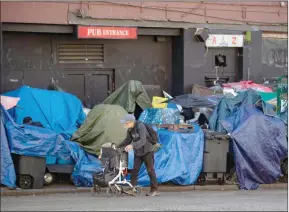  ?? ?? The Canadian Press
A man using a rolling walker passes tents set up on the sidewalk at a sprawling homeless encampment on East Hastings Street in the Downtown Eastside of Vancouver.