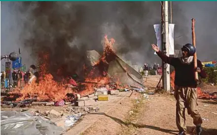  ?? REUTERS PIC ?? A protester walking near burning tents during clashes with police at the Faizabad junction in Islamabad on Saturday.