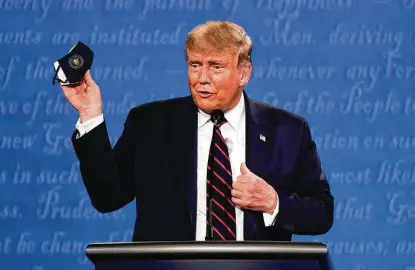  ?? Julio Cortez / Associated Press ?? Donald Trump holds up his face mask during the first presidenti­al debate at Case Western University in Cleveland, Ohio. The president and first lady Melania Trump have tested positive for the coronaviru­s.