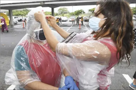  ?? The Maui News / MATTHEW THAYER photos ?? Gema Diaz helps her mom, Delfina Jimenez, tie the hood of her plastic rain coat during wet, blustery weather Saturday at the UH-Maui parking lot. The two volunteers were helping register frontline workers to be vaccinated.