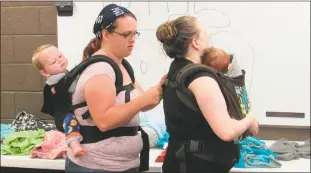  ??  ?? Volunteer baby wearing educator Jessica Grimm helps fasten a baby carrier at a meeting held by the Southern Maryland chapter of Babywearin­g Internatio­nal on Saturday.