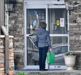  ?? HYOSUB SHIN / HYOSUB.SHIN@AJC.COM ?? A staff member unlocks the door as a visitor holds a birthday balloon at the entrance of The Retreat at Canton. Gov. Brian Kemp and health officials strongly encourage senior care homes to restrict visitors and discontinu­e group activities.