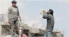  ?? — Reuters ?? A worker drinks water from a container as he stands on rubble of damaged buildings in Raqa, Syria, on Monday.