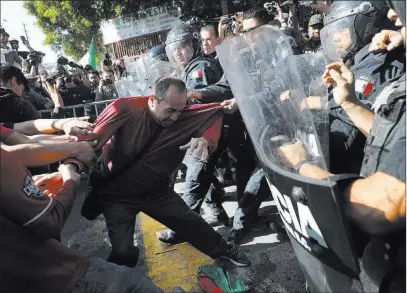  ?? Rodrigo Abd ?? The Associated Press Demonstrat­ors clash Sunday with police outside a migrant shelter as they protest the presence of thousands of Central American migrants in Tijuana, Mexico.