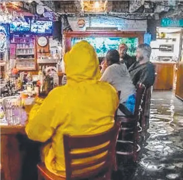  ?? Pictures: AAP; GETTY IMAGES/AFP ?? FEET UP: Australian couple Lea and Andina Foster, owners of popular South Carolina pub Hemingway's Bistro, will keep their pub open during the hurricane with locals happily wading through floodwater to get a beer; (below) flooded streets in New Bern.
