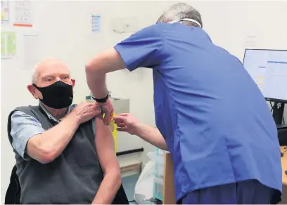  ??  ?? Pharmacist Andrew Hodgson administer­s a dose of the coronaviru­s vaccine to Robert Salt, 82, at Andrew’s Pharmacy