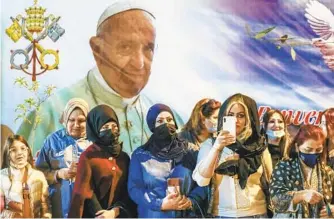  ?? ANDREW MEDICHINI AP ?? Women wait outside the Chaldean Cathedral of Saint Joseph in Baghdad, Iraq, on Saturday where Pope Francis, depicted on a giant poster at their back, was celebratin­g Mass.