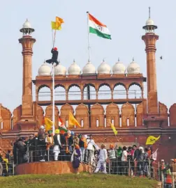  ??  ?? AT THE RED FORT on January 26, when a group of protesters tried to fix a religious flag along with a farmers’ union flag. The Indian flag flew stately behind, but a section of the media portrayed it as supplantin­g the national flag with the others.