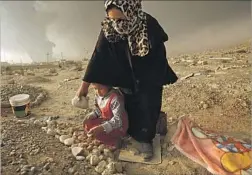  ?? Carolyn Cole Los Angeles Times ?? SIENNA MOQTAR and her daughter use rocks to adorn the grave of Moqtar’s brother in Qayyarah. He was slain last week as Iraq began its offensive.