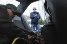  ?? AP ?? Uber driver Luis Hidalgo, wearing a face mask, watches as Joel Rios installs a plastic barrier in his car to protect himself and his passengers from the new coronaviru­s in New York.