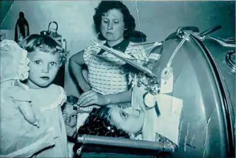  ?? Photos courtesy of Bonny Kehm ?? Bonny Kehm’s mother, in the foreground with her doll, stands next to her sister Lillian in an iron lung. Their mother stands in the background.