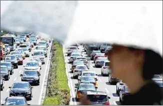  ??  ?? A woman walks past vehicles on a city ring-road clogged with heavy traffic in Beijing, Aug 13. China’s auto sales
sank again in July, extending a yearlong contractio­n in the industry’s biggest global market. (AP)