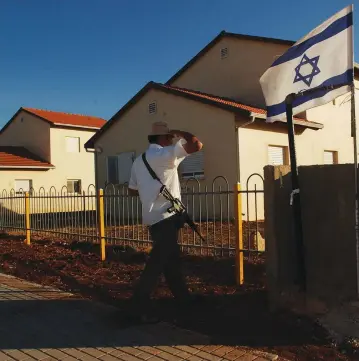  ?? (Flash90) ?? AN ARMED MAN looks at the Israeli flag in the settlement of Rehelim in 2002, whose founders included nowPeace Now activist Shabtay Bendet.