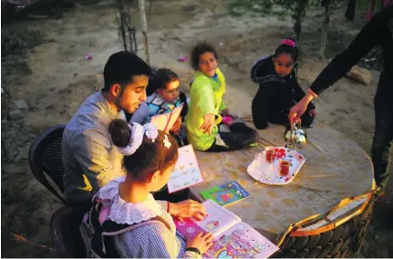  ?? Photos Mohammed Abed / AFP ?? Mosab Abu Toha, who is collecting English books for his librarypro­ject in Gaza, reads with children in the garden at his family home in Beit Lahia in northern Gaza. Below, friend and fellow bibliophil­e Shafi Salem is helping out.