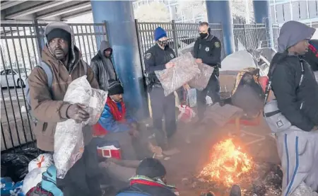  ?? JON SHAPLEY/HOUSTON CHRONICLE ?? Police officers Kenneth Bigger, center, and Aaron Day hand out blankets to people Tuesday under Interstate 45 in Houston.