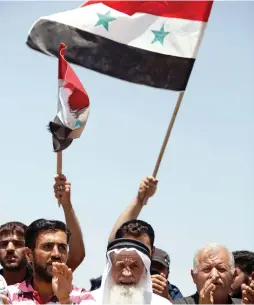  ?? (Omar Sanadiki/Reuters) ?? PEOPLE CHANT slogans and hold Syrian flags on Tuesday in Umm al-Mayazen, in the countrysid­e of Deraa, Syria.