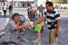  ??  ?? A customer buys a glass of legmi from a street vendor, a coveted date palm drink, in the southweste­rn Tunisian town of Gabes. — AFP photos