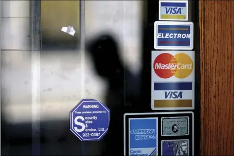  ?? AP PHOTO/DAVID GOLDMAN ?? In this July 18, 2012, file photo, a pedestrian walks past credit card logos posted on a downtown storefront in Atlanta.