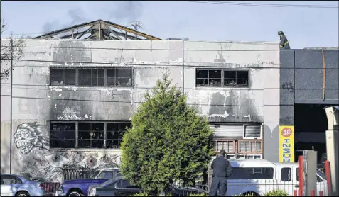  ?? JOSH EDELSON / ASSOCIATED PRESS ?? A firefighte­r walks on the roof of a smoldering former warehouse in Oakland, Calif., after a fire tore through a dance party there early Saturday. Officials fear dozens might have died while trapped inside.