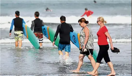  ??  ?? On high alert: Tourists walking past surfers along Kuta beach in Denpasar, Bali.