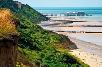  ??  ?? The cliffs roll down to meet the beach, with the pier, culminatin­g in its theatre and lifeboat station, in the distance.