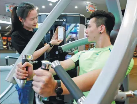  ?? XINHUA ?? A man looks at data displayed by a mobile phone app, which tracks the time and energy consumed while he does exercise in a gym in Beijing.