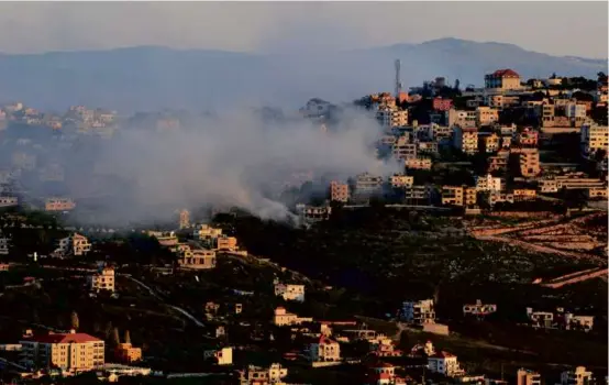  ?? RABIH DAHER/AFP VIA GETTY IMAGES ?? Smoke rose over buildings on the outskirts of the Lebanese border village of Khiam after an Israeli airstrike on Sunday. At left, friends gathered in Karmiel, Israel, for the funeral of a border police officer killed when her vehicle hit a buried explosive device.