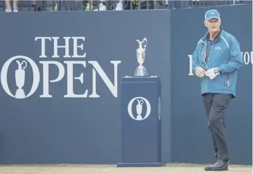  ??  ?? 0 Sandy Lyle walks past the claret Jug to the first tee at 6.35 yesterday morning, watched by a large crowd of appreciati­ve fans.